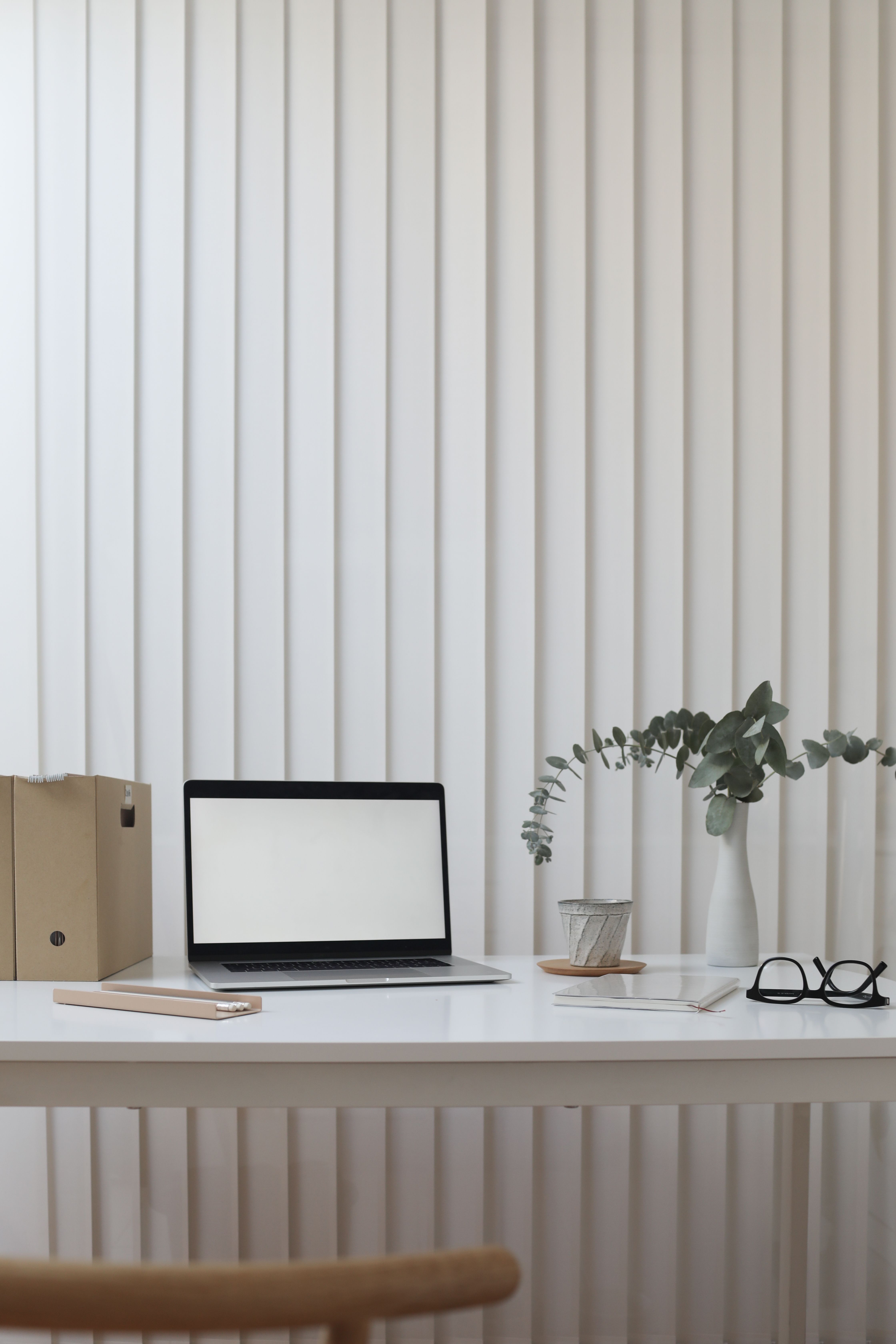 A tidy, minimalist office desk with a closed laptop, notebook, glasses, and a small plant.
