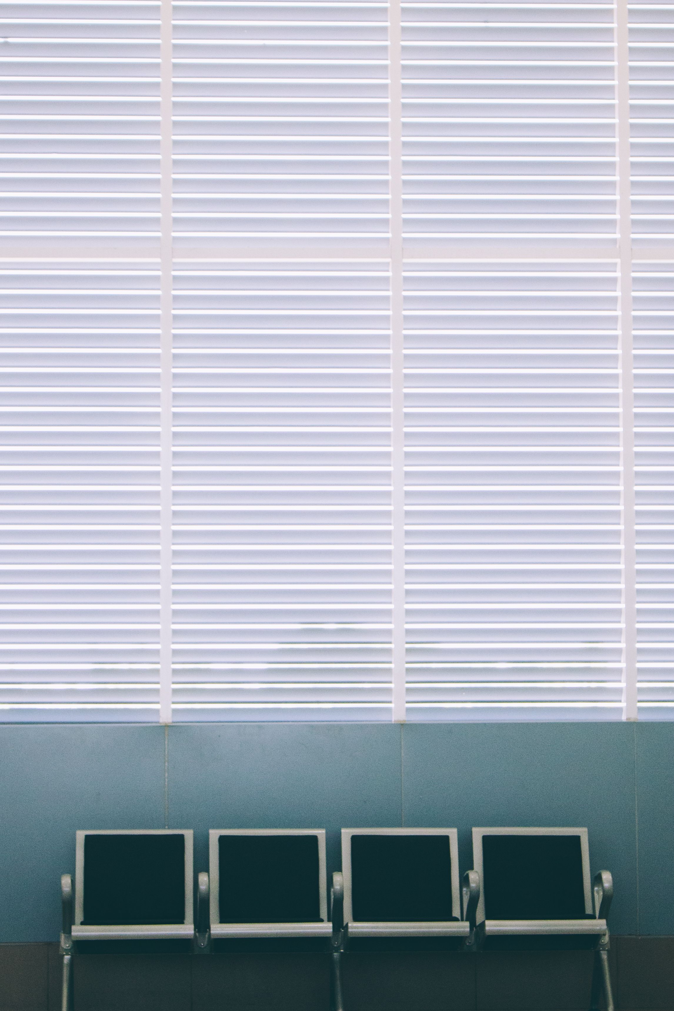 Empty row of waiting-room chairs against a wall of white venetian blinds.